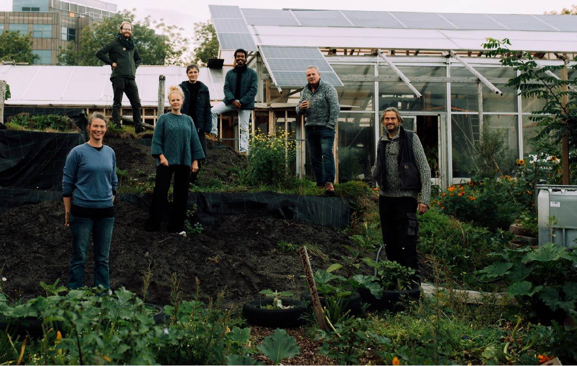 Mensen in een groene omgeving met op de achtergrond een kas met zonnepanelen