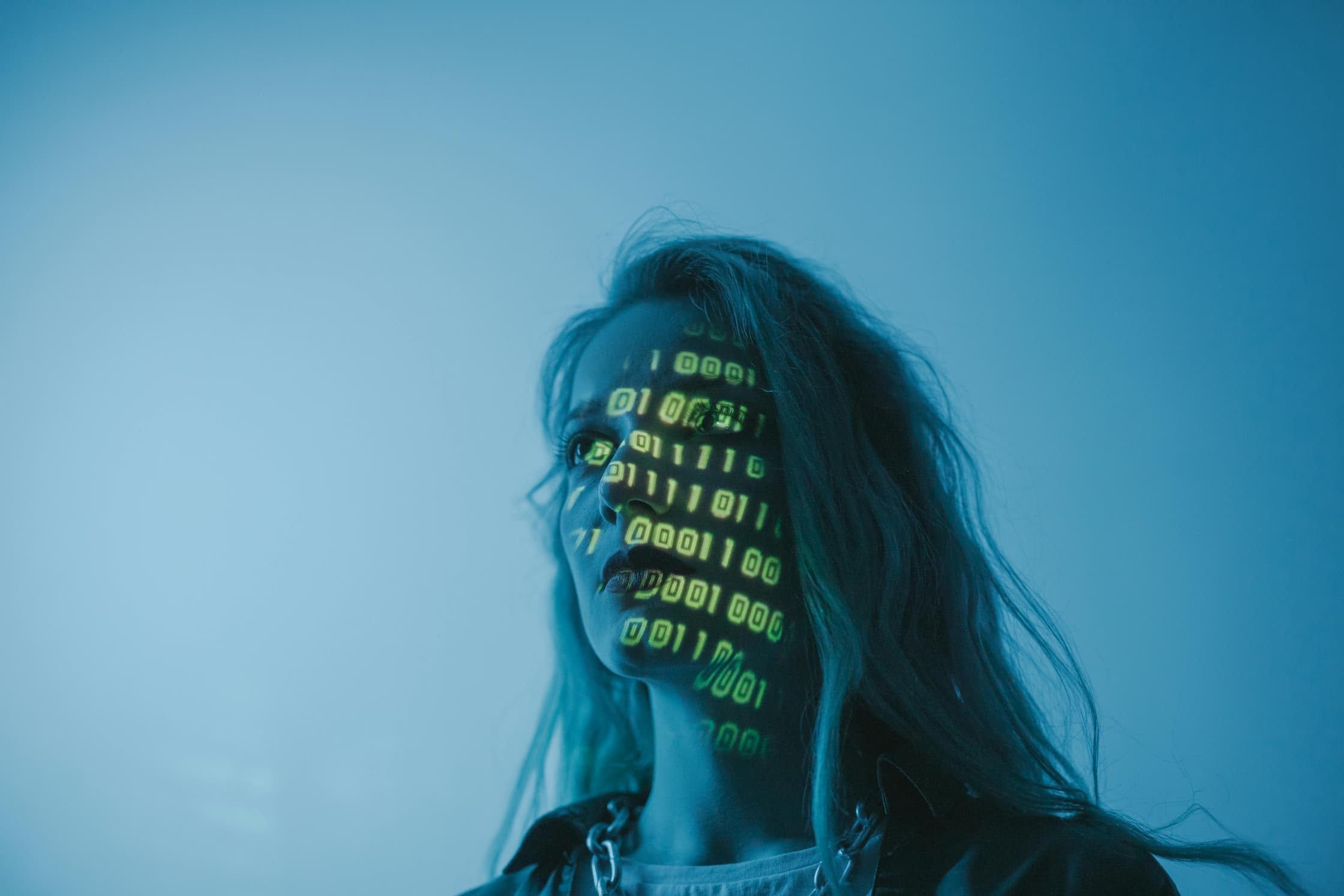 Tegen een lichtblauwe achtergrond zien we het hoofd van een vrouw die schuin naar links te camera in kijkt. Over haar gezicht worden digitale cijfers geprojecteerd in lichtgroen.