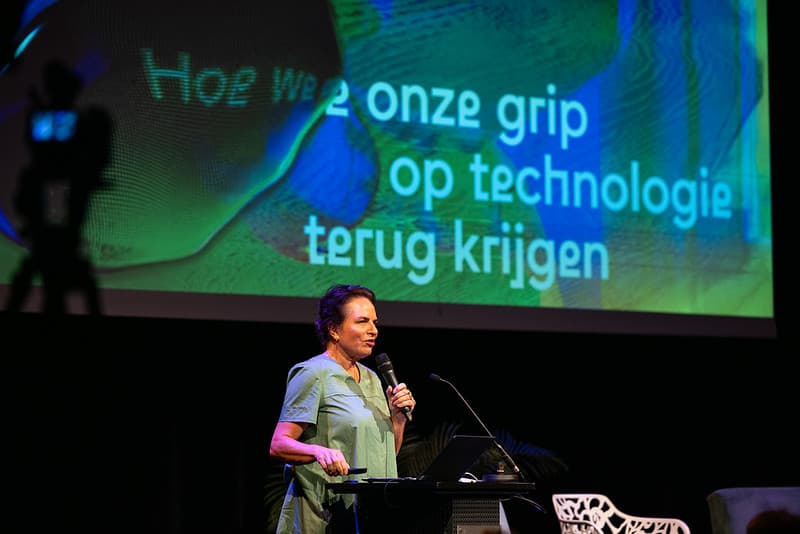 Marleen Stikker spreekt voor een projectiescherm met daarop Hoe we onze grip op technologie terug krijgen