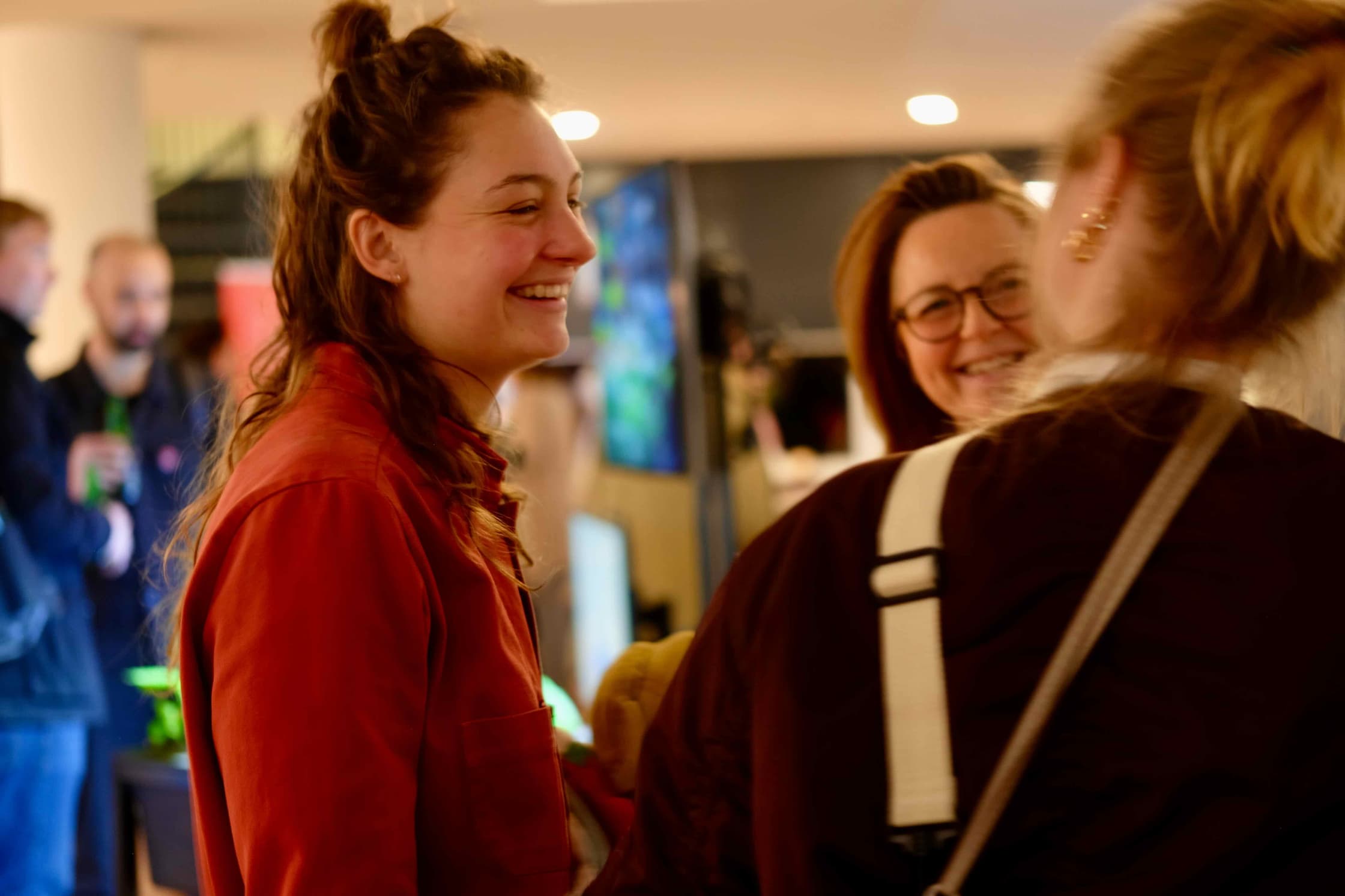 Foto van een groep pratende mensen tijdens een workshop. Een vrouw in een rode trui kijkt lachend naar de persoon rechts naast haar, die met de rug naar de camera toe staat.