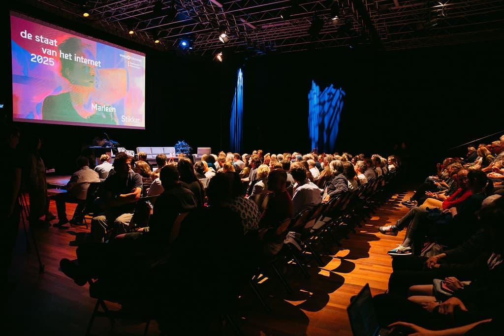 Publiek zit voor groot scherm tijdens Staat van het Internet lezing