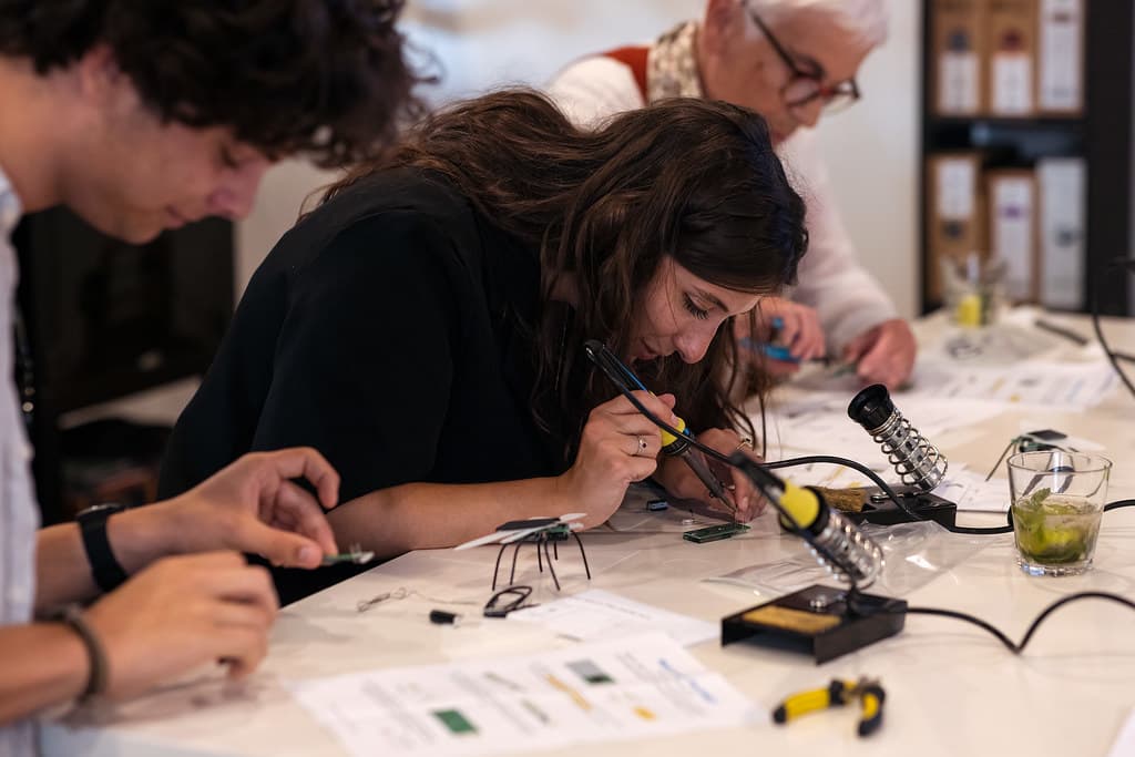 Drie mensen zittend aan tafel en aan het solderen. 