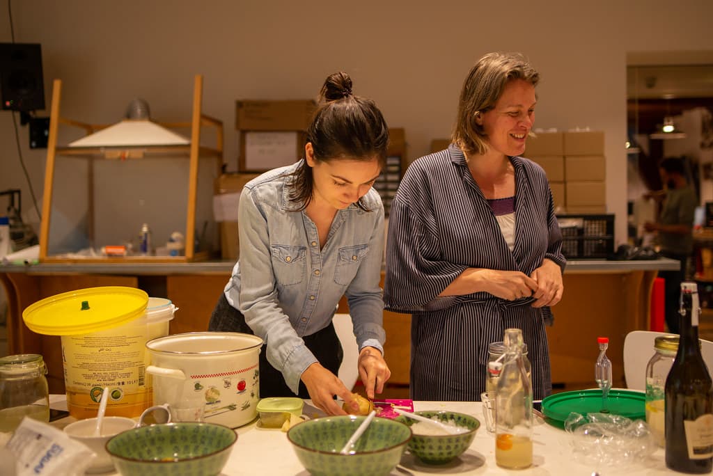 Twee vrouwen achter een tafel met ememrs, potten en spullen voor fermentatie